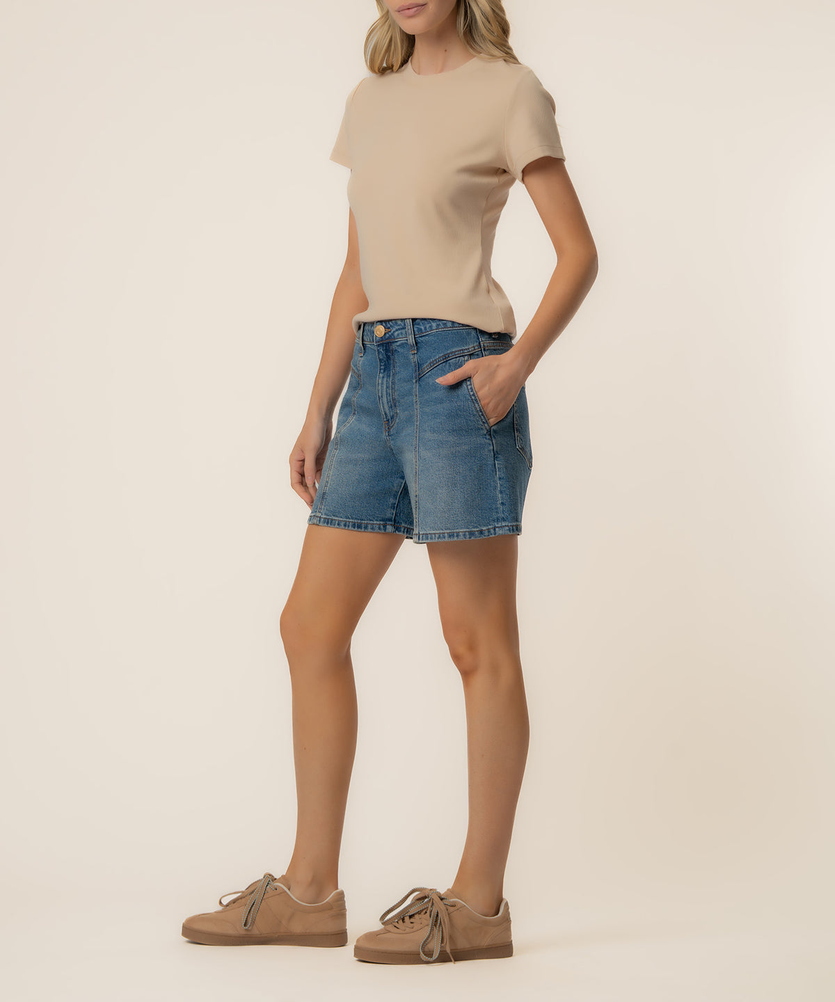Woman wearing beige t-shirt and high-rise denim shorts in medium wash with front pockets.