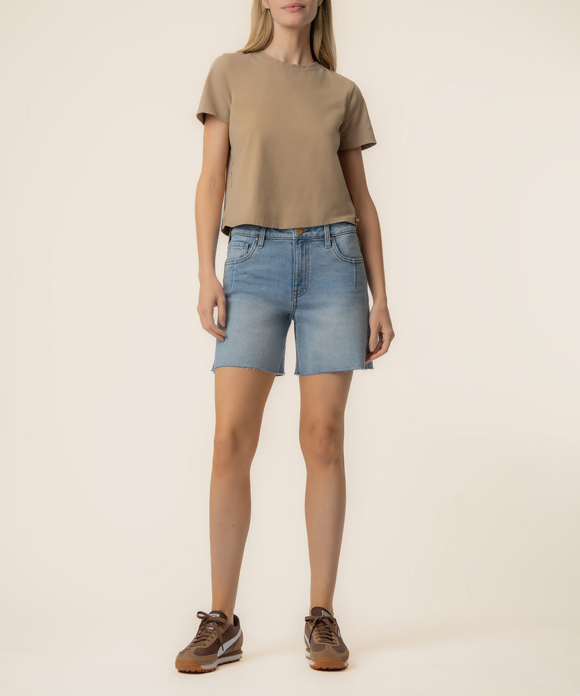 Woman wearing light blue denim high-rise shorts with raw hem and tan t-shirt.