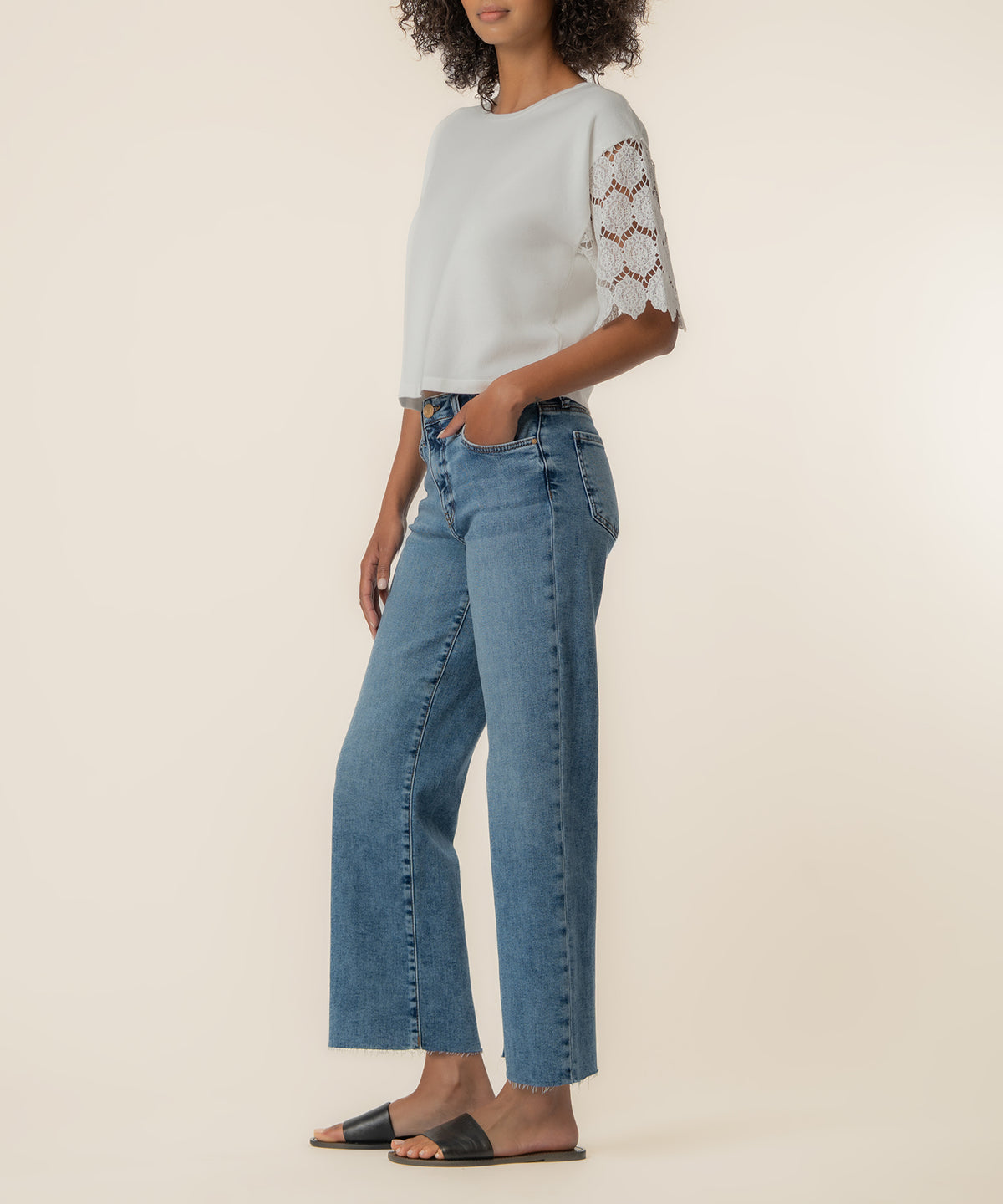 White knit top with lace sleeves paired with blue denim jeans and black slide sandals.