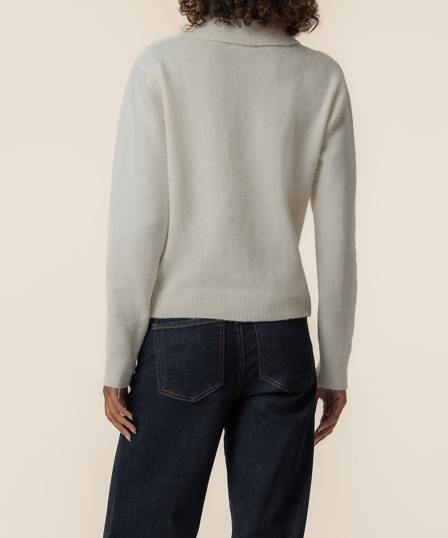 Cream knit sweater with long sleeves and ribbed trim worn with dark denim jeans, shown from back view.