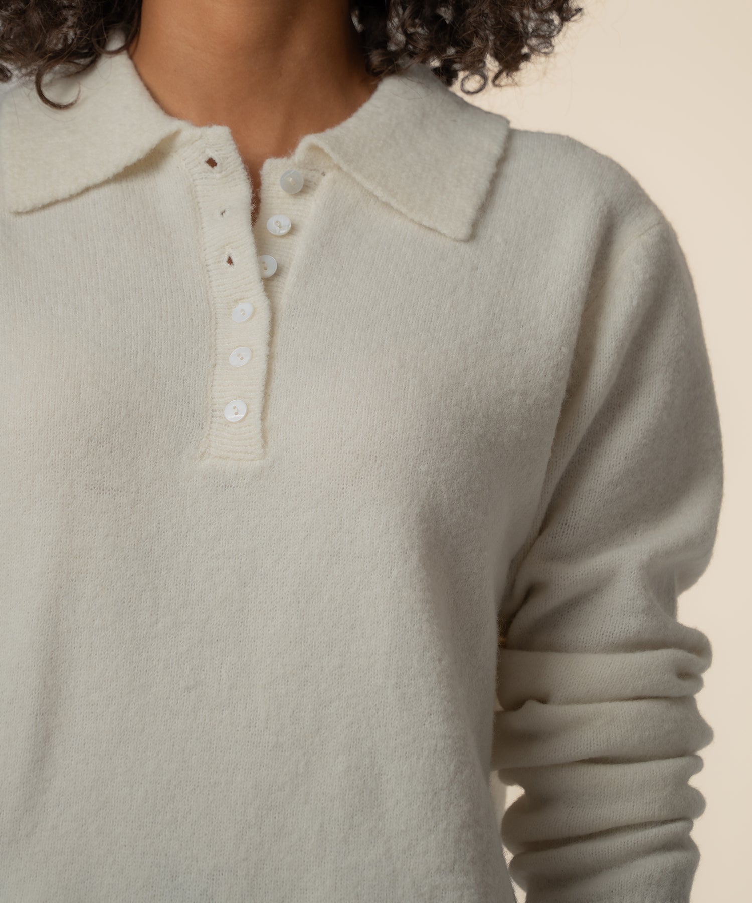 Cream-colored sweater with collared neckline and white button placket front, shown on model with dark curly hair.