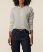 Cream polo-style sweater with long sleeves and ribbed cuffs, worn with dark denim jeans.