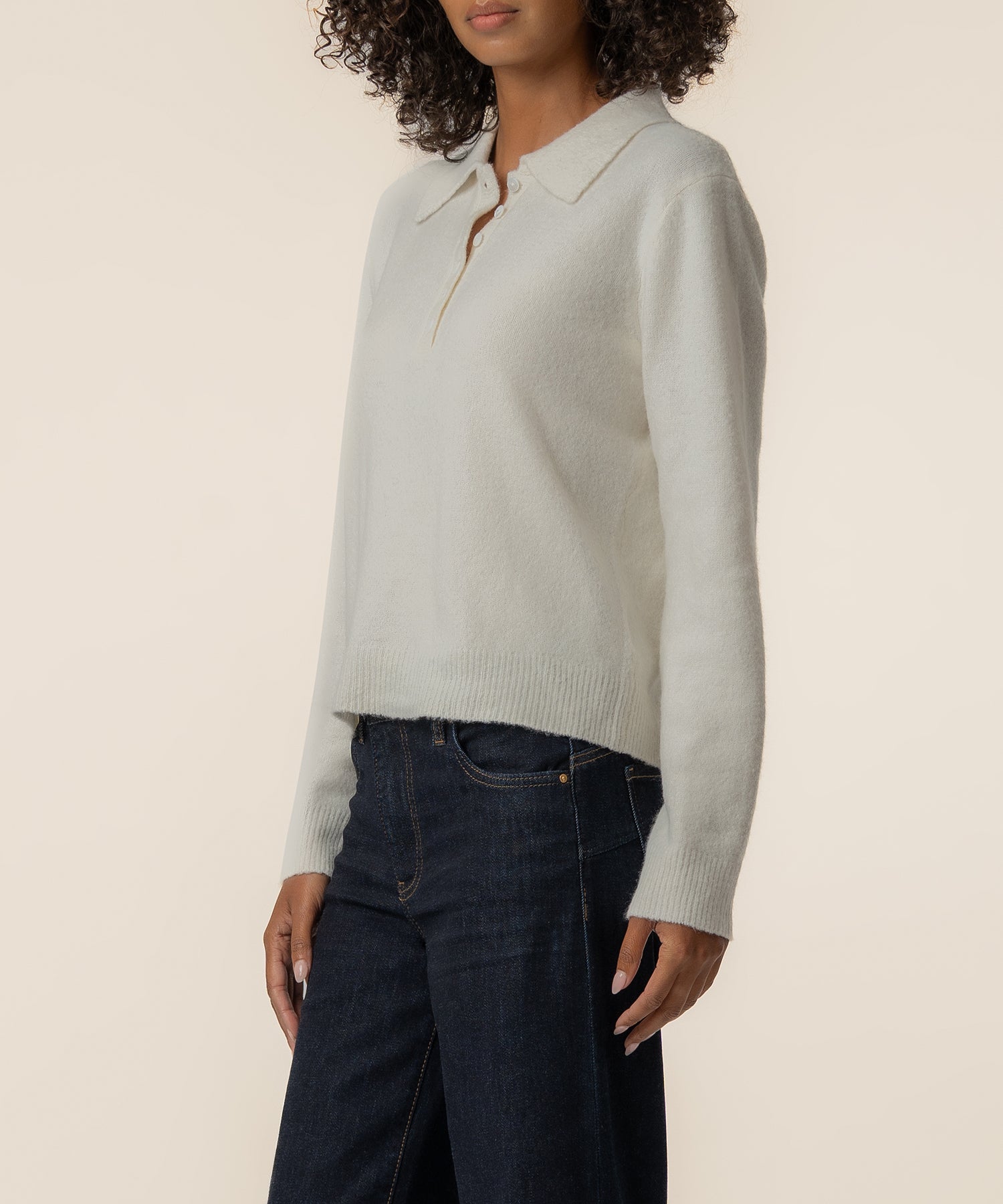 Cream-colored polo sweater with ribbed cuffs and hem, worn with dark denim jeans.