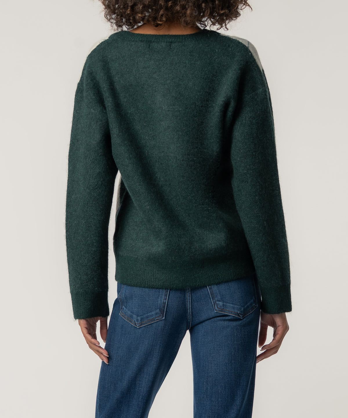 Back view of a person with curly hair wearing a dark green knit sweater with long sleeves and blue jeans.