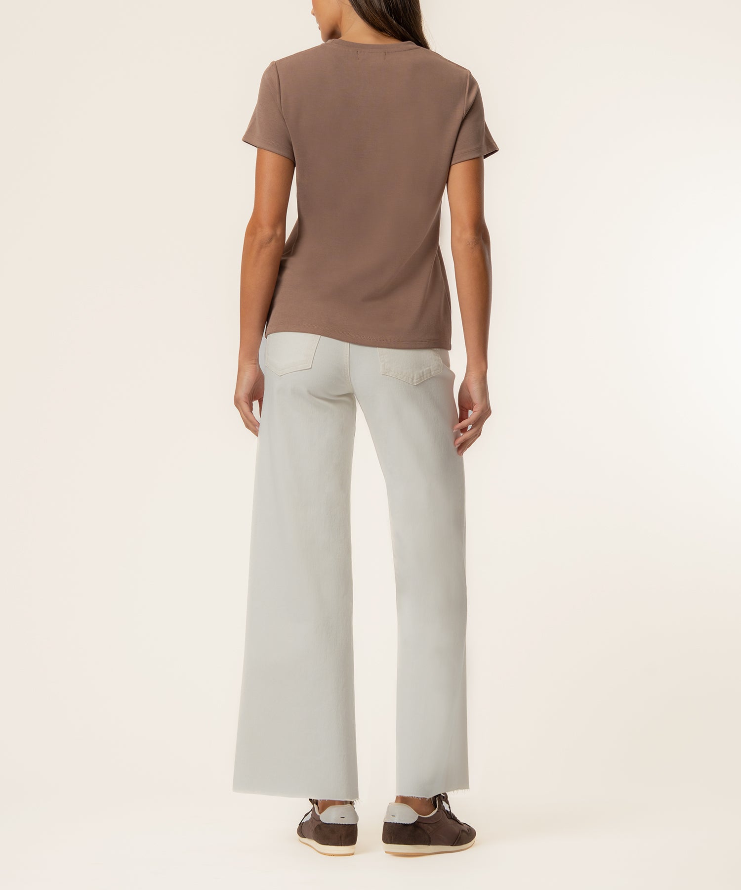 Woman wearing a taupe short-sleeve t-shirt and cream-colored wide-leg jeans, shown from behind.
