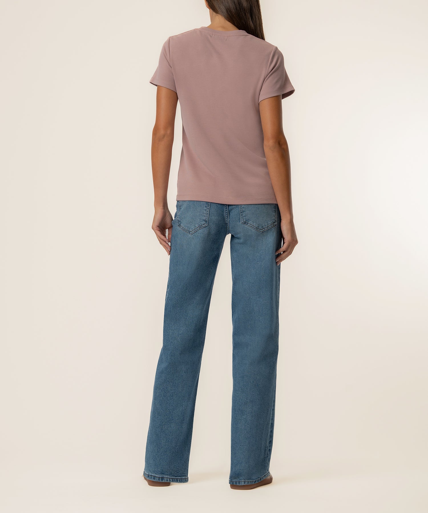 Woman wearing vintage rose short-sleeve t-shirt and blue jeans, shown from back.