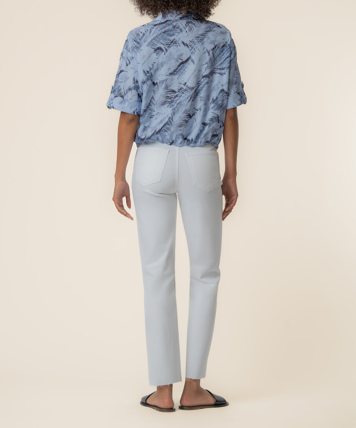 Person wearing light blue feather-print short-sleeve shirt and white cropped jeans, shown from back.