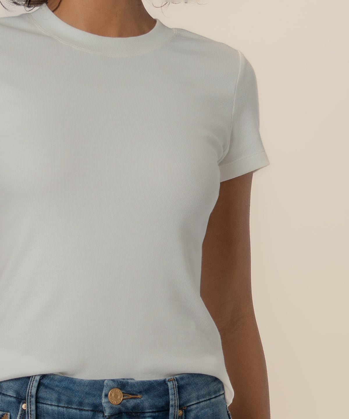 White ribbed short-sleeve crew neck top worn with blue jeans.