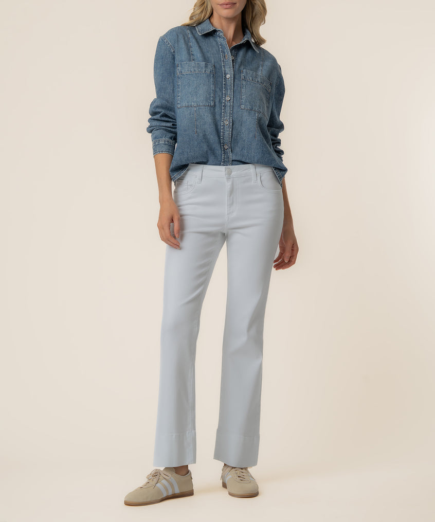 Woman wearing a light blue denim button-up shirt with chest pockets, paired with white flared jeans and tan sneakers.