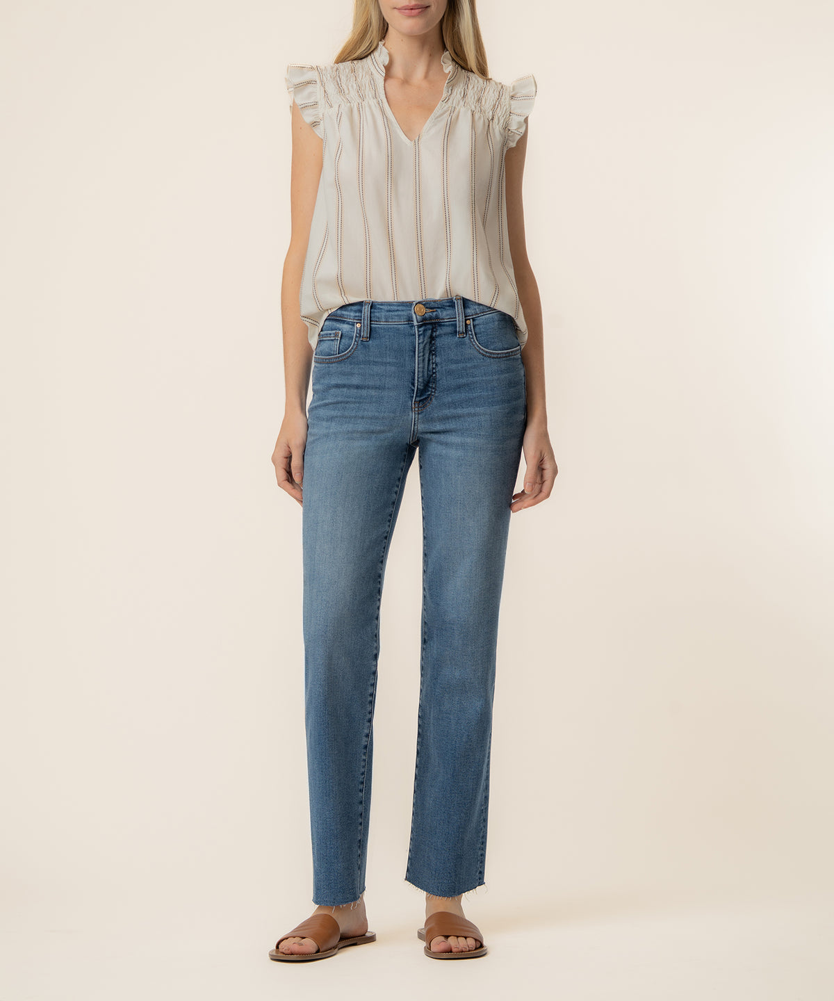 Cream sleeveless top with ruffled neckline and vertical stripes, worn with blue jeans and brown sandals.