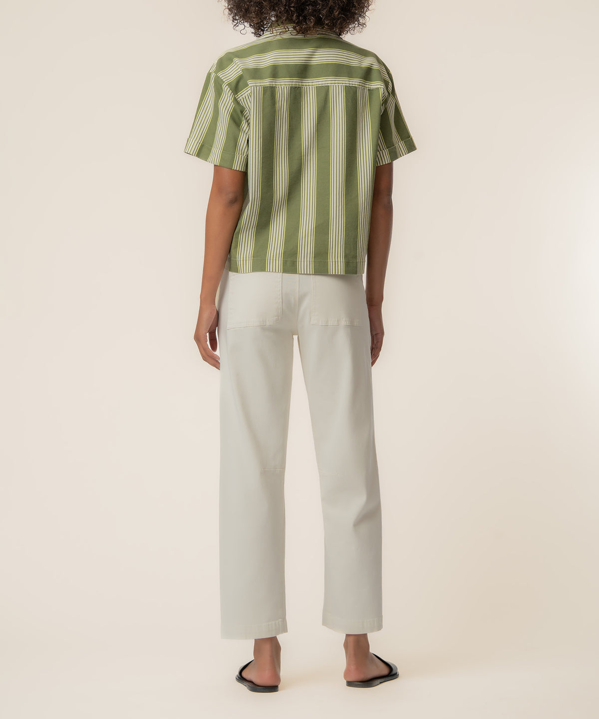 Woman wearing olive and ivory striped short-sleeve linen top with ivory straight-leg pants, shown from back view.