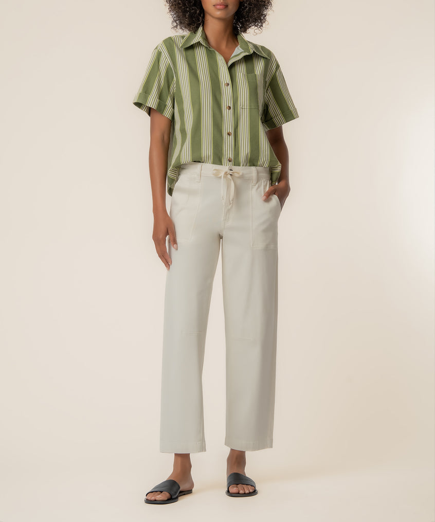 Woman wearing olive and ivory striped short-sleeve button-up top with ivory drawstring pants and black slides.