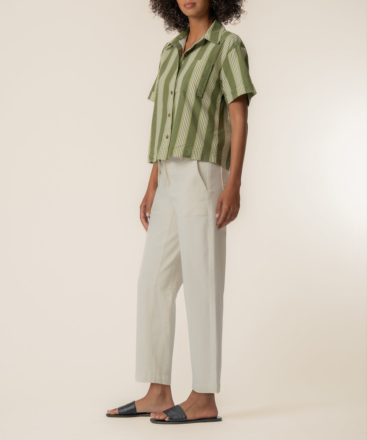 Olive and ivory striped linen button-up shirt with short sleeves worn with ivory trousers.