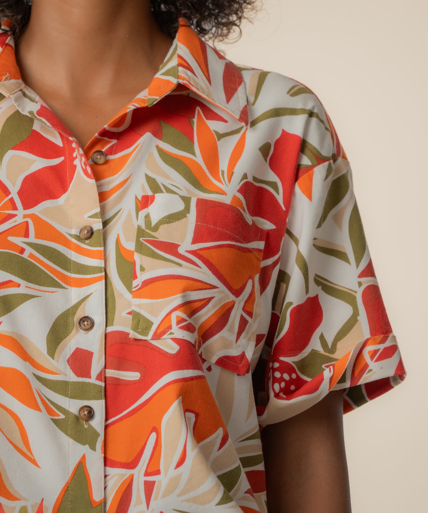 Short-sleeved linen top with red, orange, and olive leaf print on cream background, button front closure.
