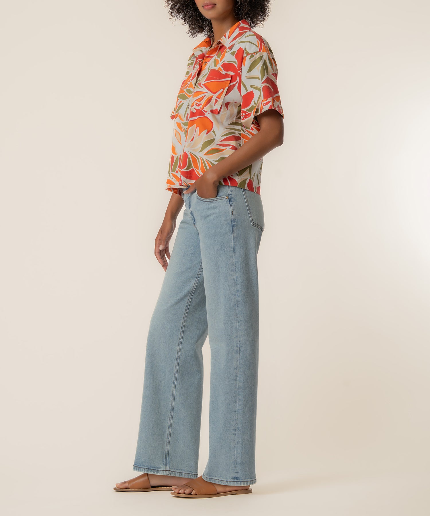 Woman wearing red and orange floral print linen top with short sleeves paired with light blue denim jeans.