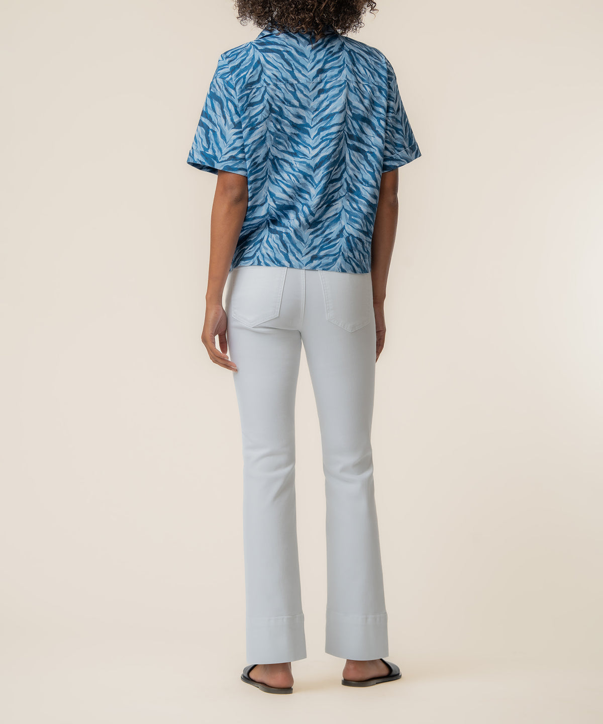 Navy blue linen top with zebra stripe pattern, shown from back on model wearing white flare pants.
