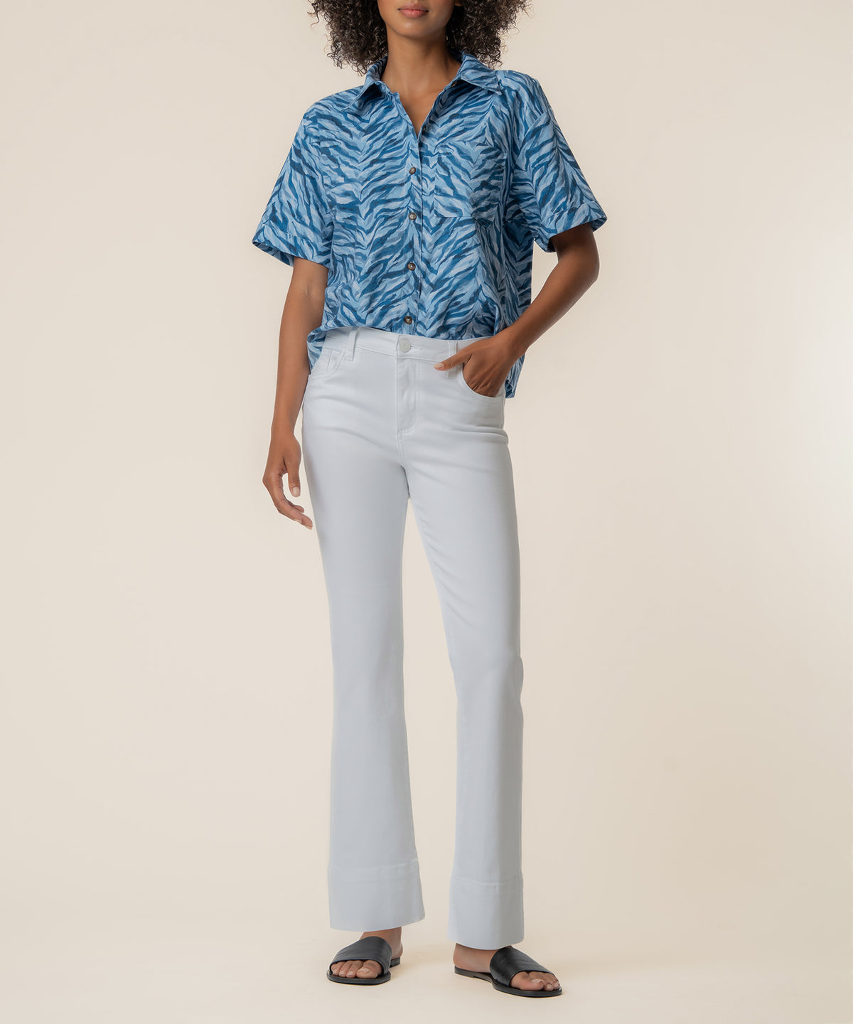 Woman wearing navy blue zebra-striped linen short-sleeve button-up shirt with white trousers and black sandals.