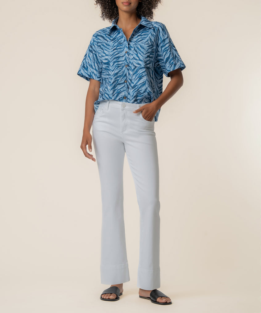 Woman wearing navy blue zebra-striped linen short-sleeve button-up shirt with white trousers and black sandals.
