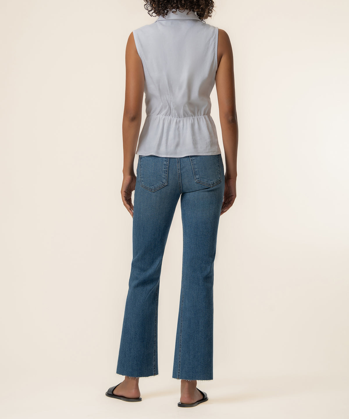 White sleeveless linen top with cinched waist, styled with blue denim flare jeans.