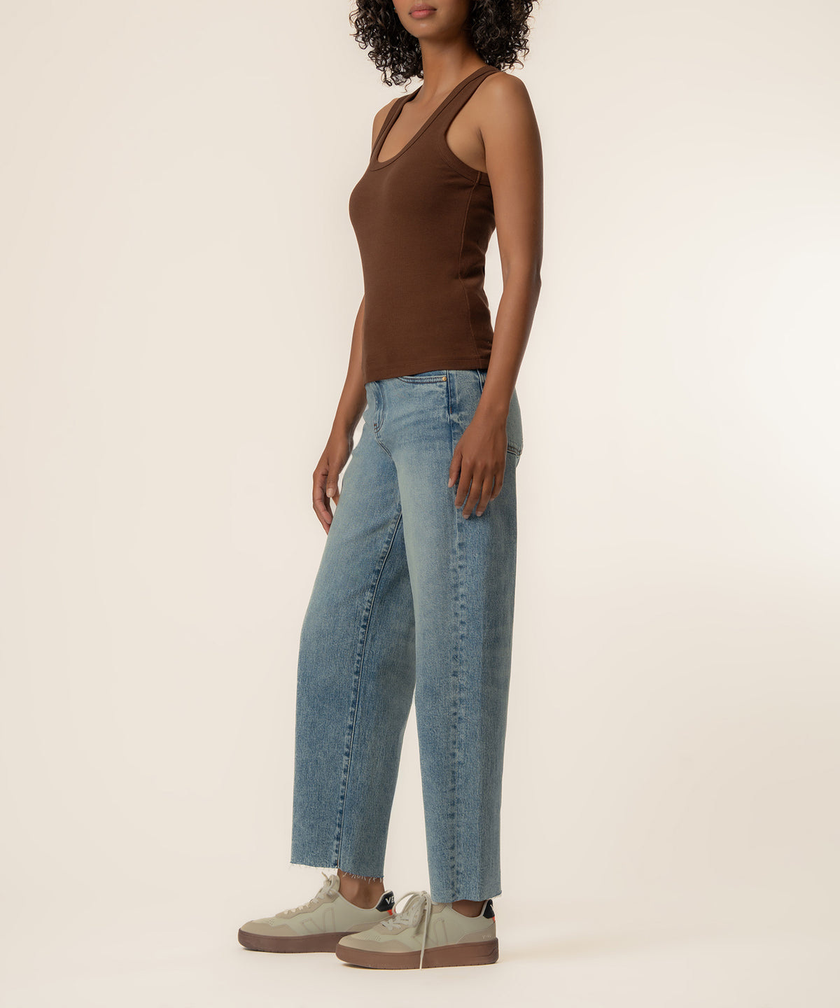 Woman wearing brown sleeveless tank top with scoop neckline, paired with light blue jeans and cream sneakers.