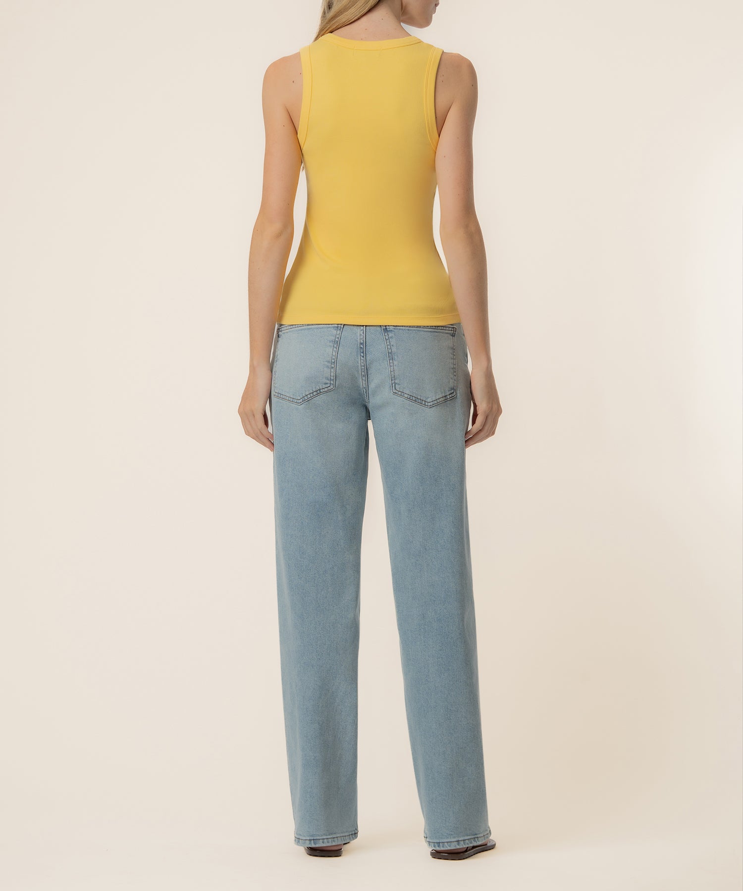 Woman wearing yellow sleeveless tank top and light blue denim jeans, shown from back view.