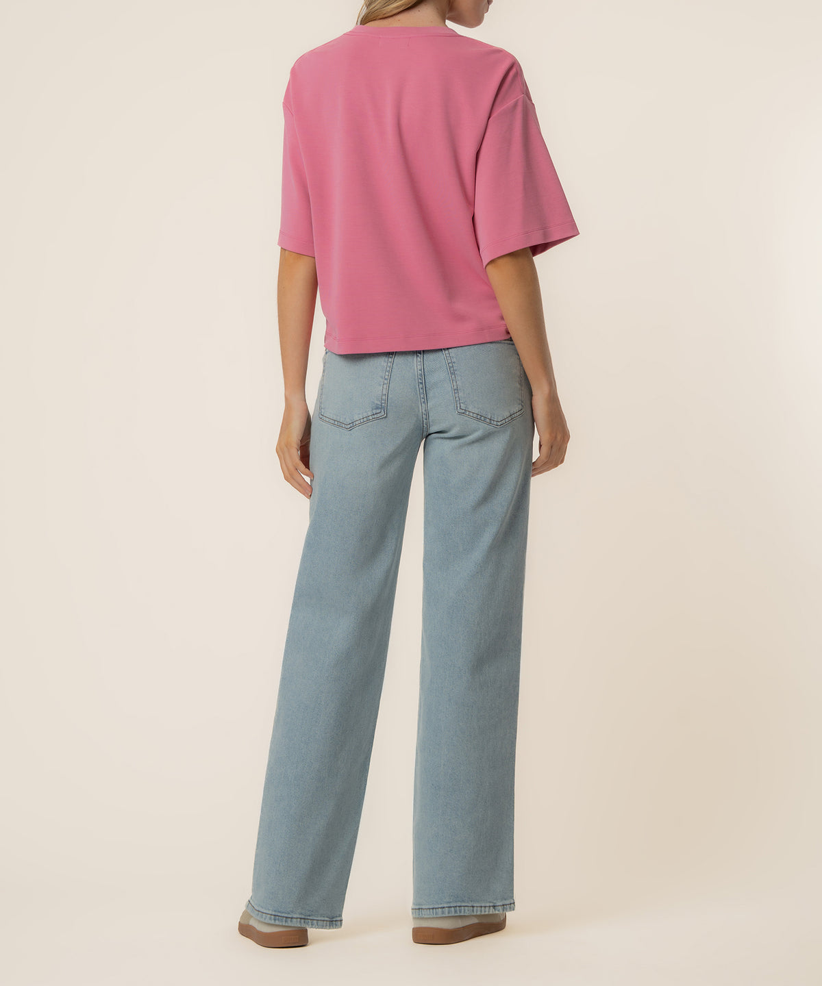 Woman wearing a pink boxy short-sleeve tee and light blue straight-leg jeans, back view.