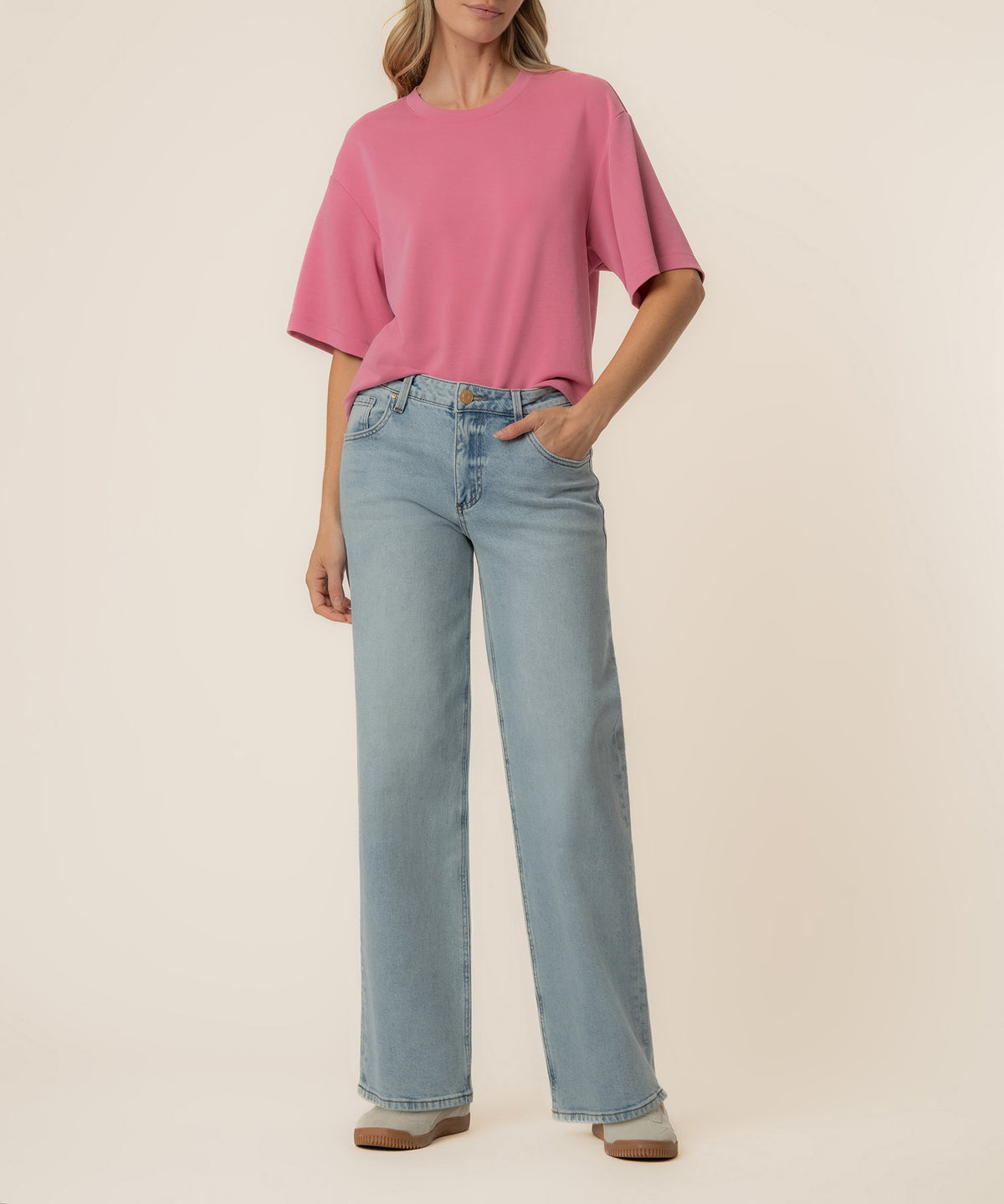 Woman wearing a pink boxy short-sleeve tee with light blue straight-leg jeans and tan slip-on shoes.