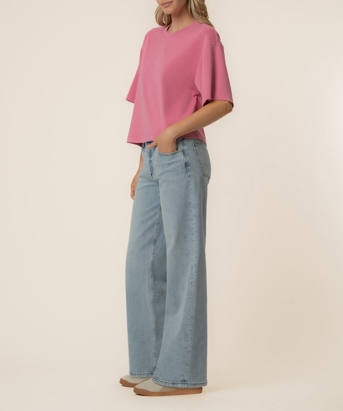 Woman wearing a pink boxy short-sleeve tee with light blue wide-leg jeans and tan slip-on shoes.