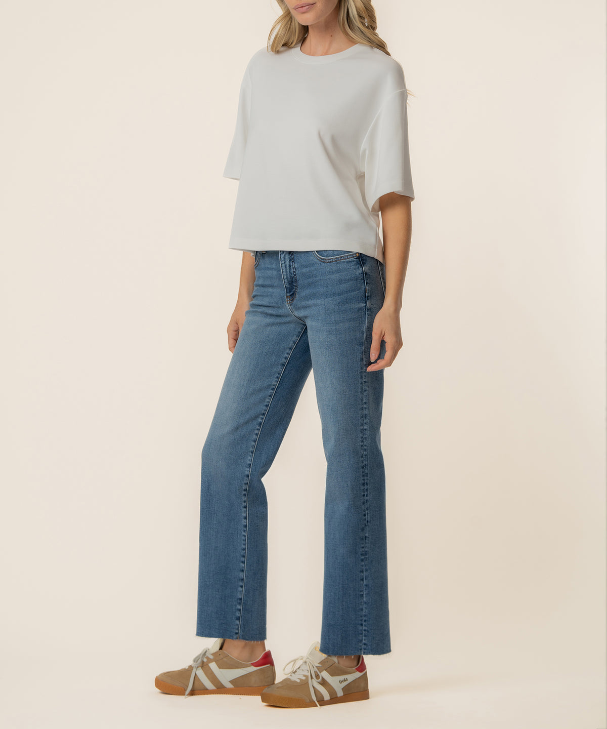 Woman wearing a white boxy short-sleeve tee with blue denim jeans and tan lace-up sneakers.