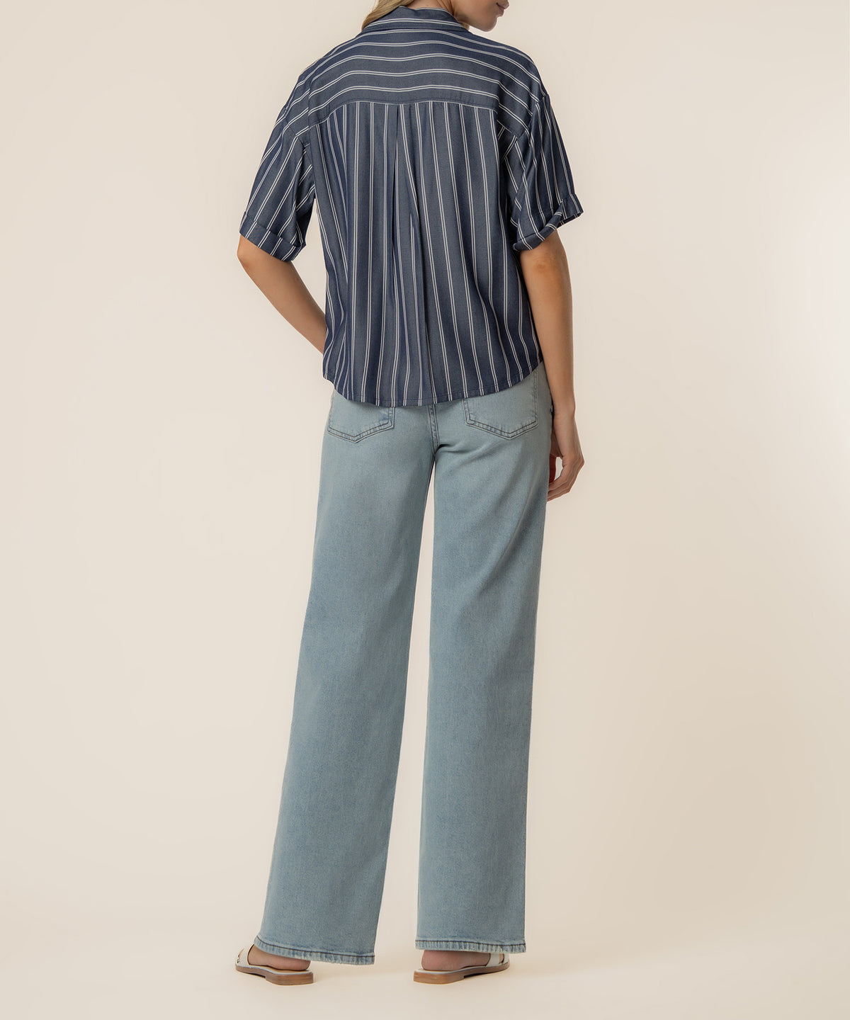 Navy and white striped button-up shirt with short sleeves and boxy fit worn with light blue jeans.