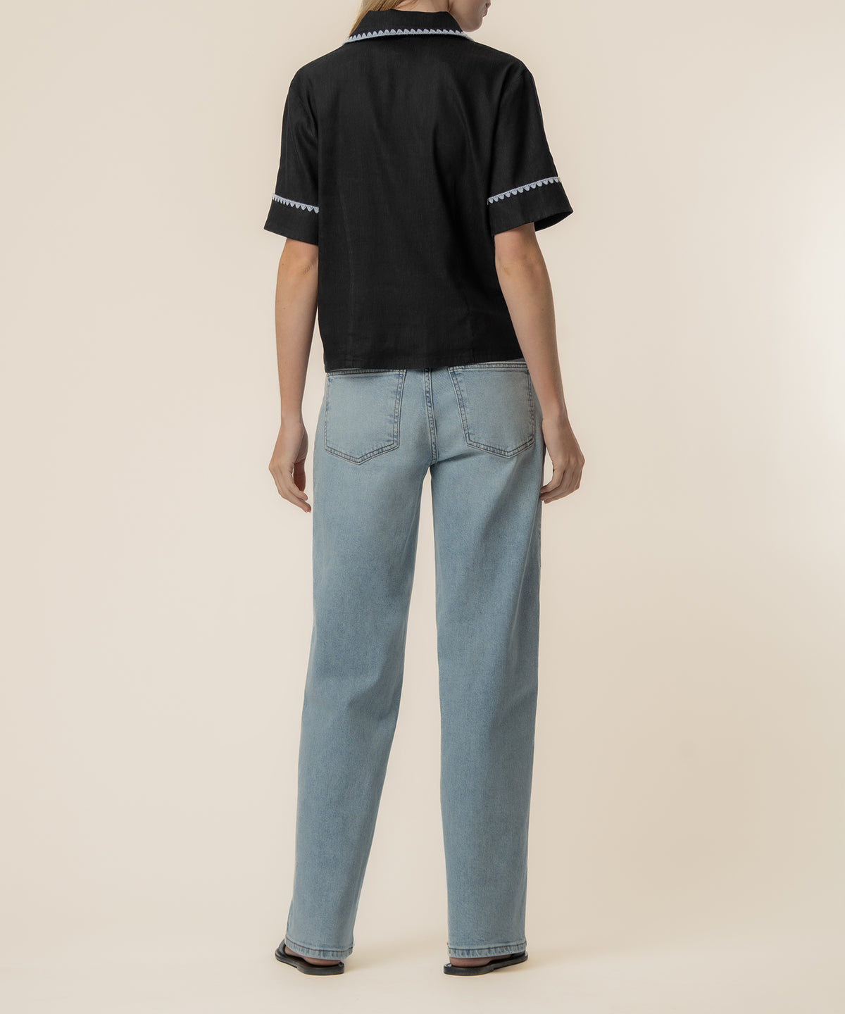 Black linen top with white trim on collar and sleeves, shown from back on model wearing light wash jeans.