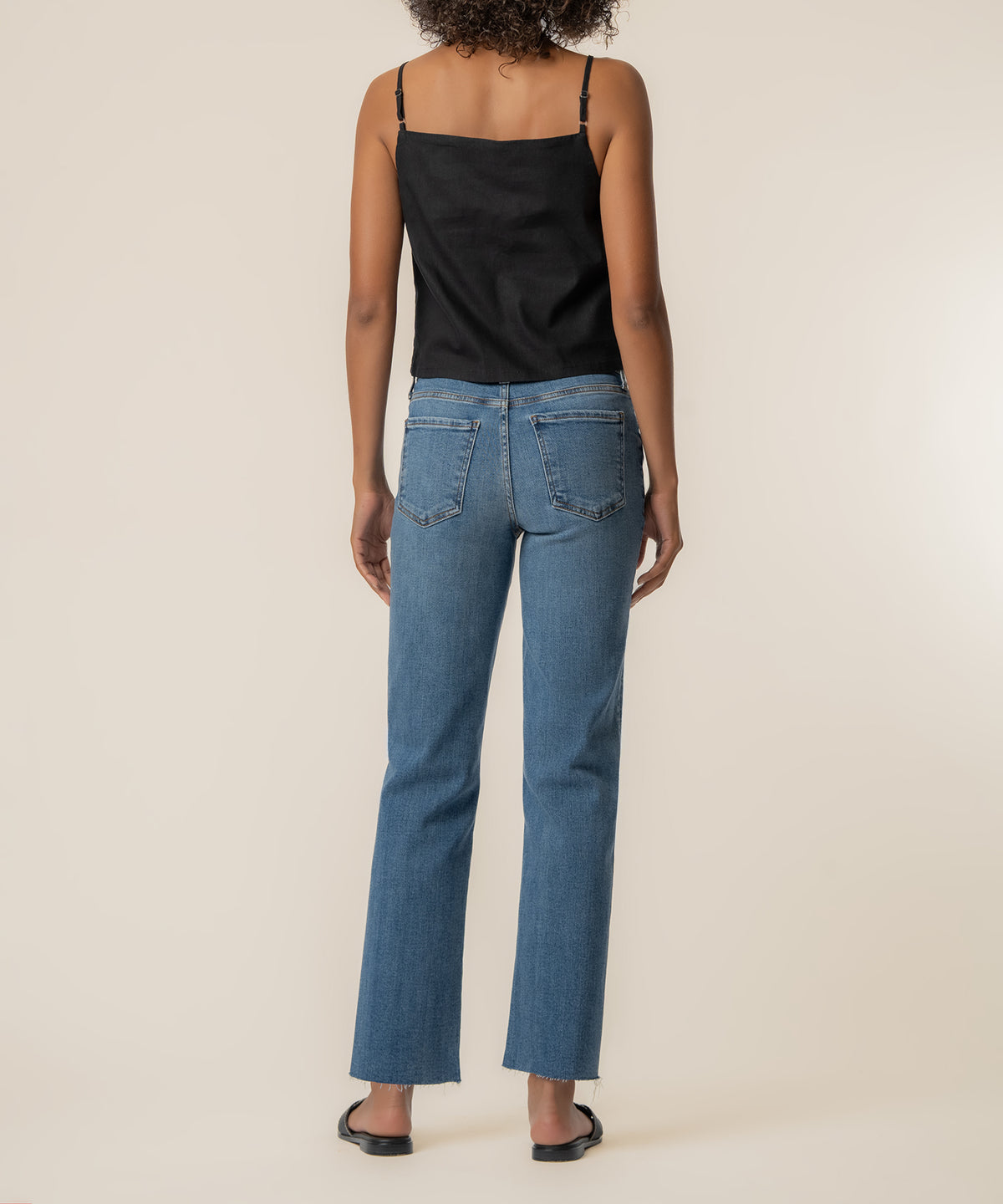Black spaghetti strap camisole top shown from back view worn with blue denim jeans.