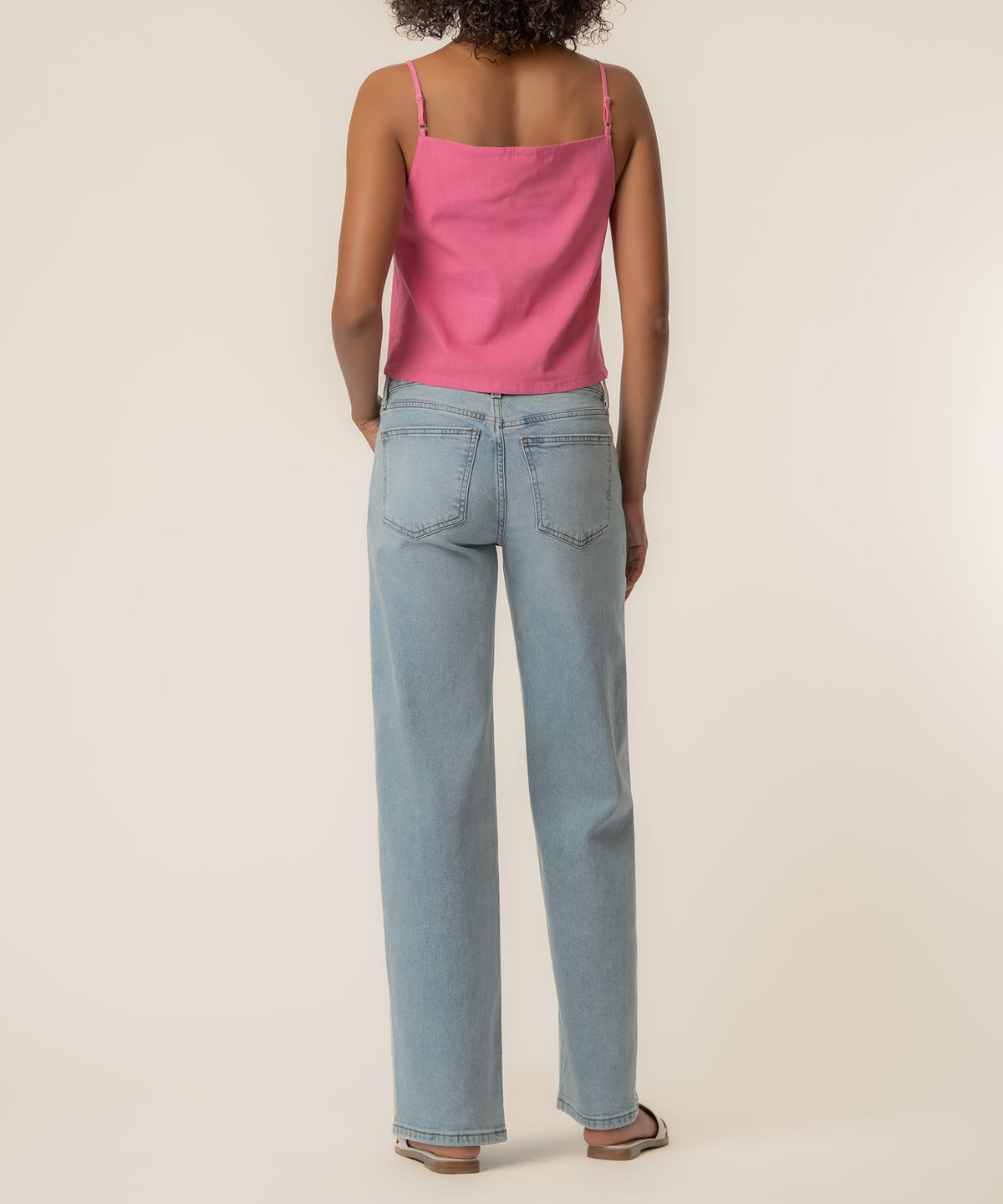 Pink spaghetti strap top with thin shoulder straps shown from back, paired with light blue straight-leg jeans.
