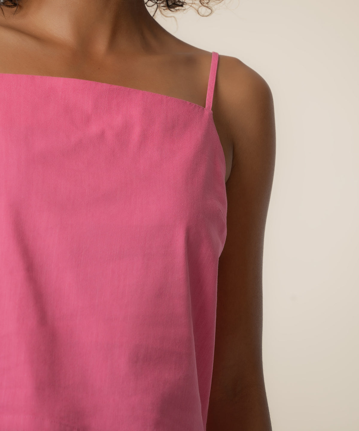 Pink spaghetti strap top with thin shoulder straps on model against neutral background.