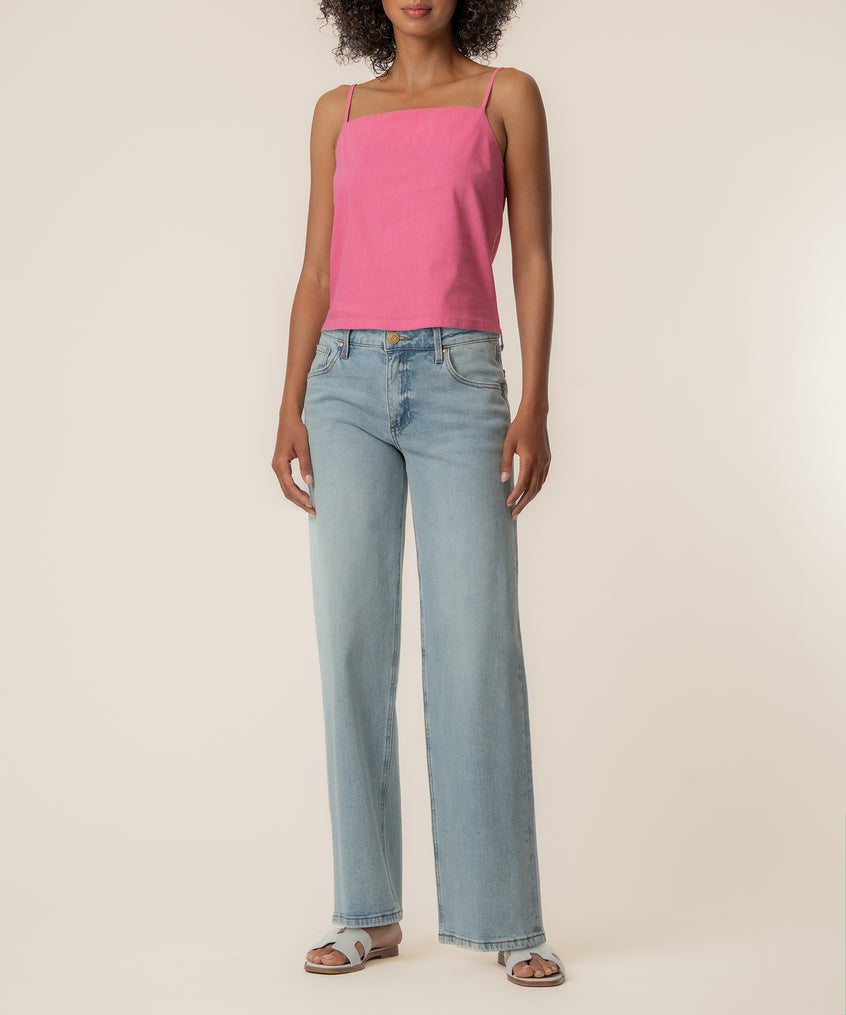 Woman wearing a pink spaghetti strap top with light blue jeans and brown sandals.