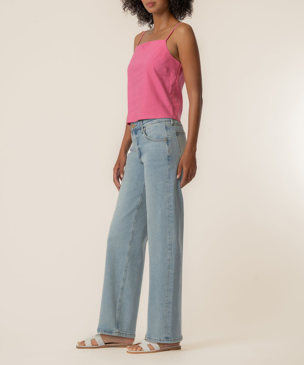 Woman wearing pink spaghetti strap top with light blue jeans and white striped sandals.