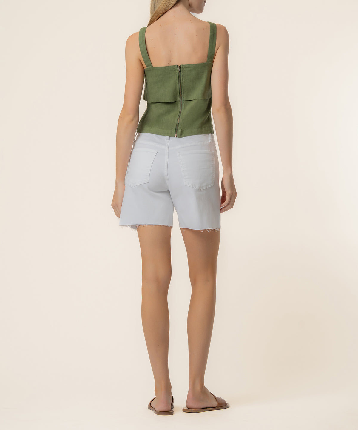 Woman wearing olive linen tank top with back zip closure and white denim shorts, viewed from behind.