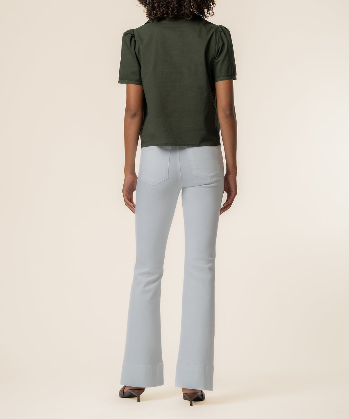 Olive short-sleeve top with cropped length worn with light blue flare jeans, back view.