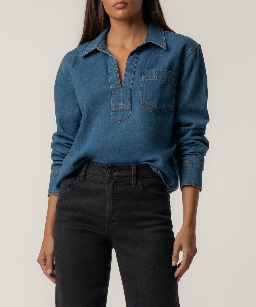 Medium-wash denim shirt with collar, front pocket, and half-button placket worn with black jeans.